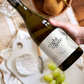 A hand holding a bottle of Eight at the Gate Family Selection Chardonnay Single Vineyard 2019 over a cheese board.
